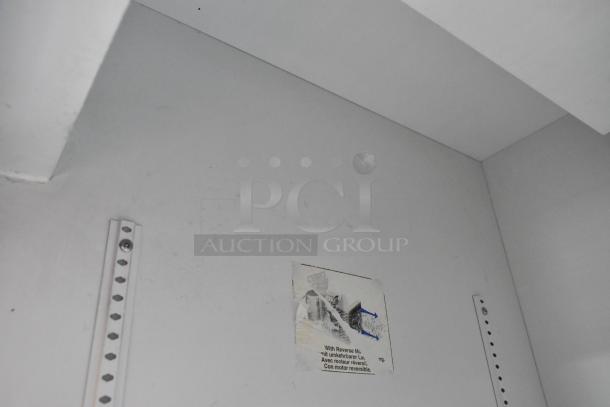 "Interior of True Metal Commercial 2 Door Reach In Cooler Merchandiser, white walls, shelving brackets visible, label partially torn."