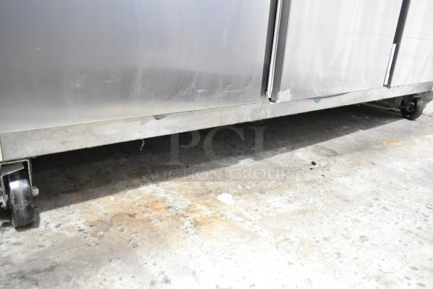 2018 Traulsen G30010 stainless steel 3-door reach-in cooler with poly-coated racks on casters. Left and right doors locked.