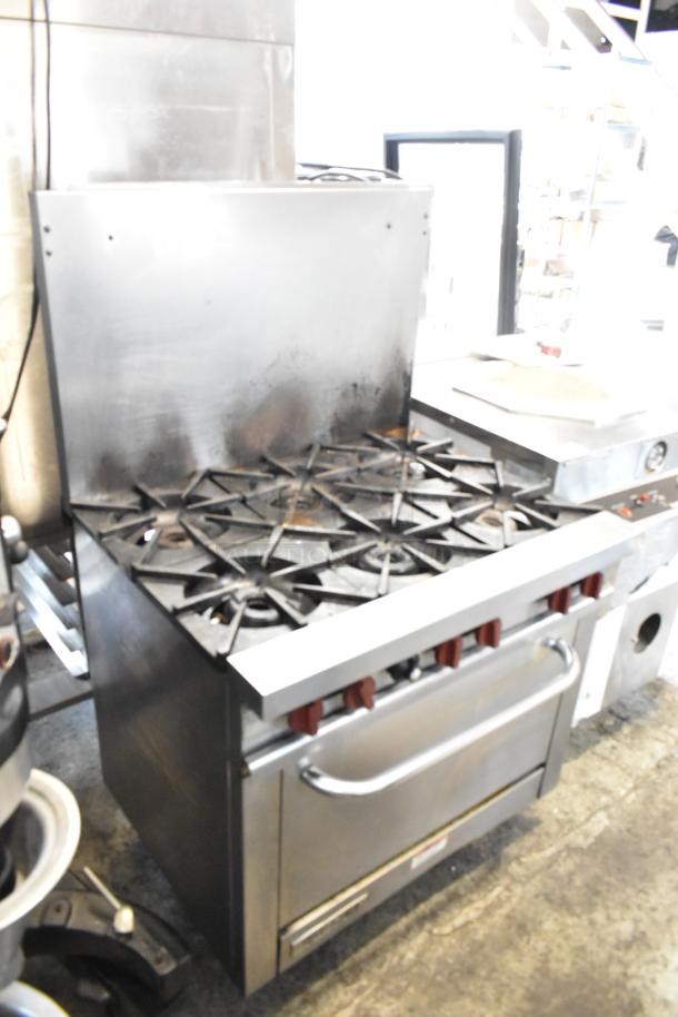 Vulcan stainless steel commercial gas-powered 6 burner range with oven and backsplash. Visible wear on surfaces.