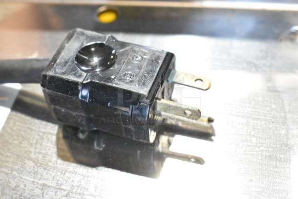 A close-up of a plug for the Unic Phoenix MI Stainless Steel Espresso Machine, showing wear on metal prongs.