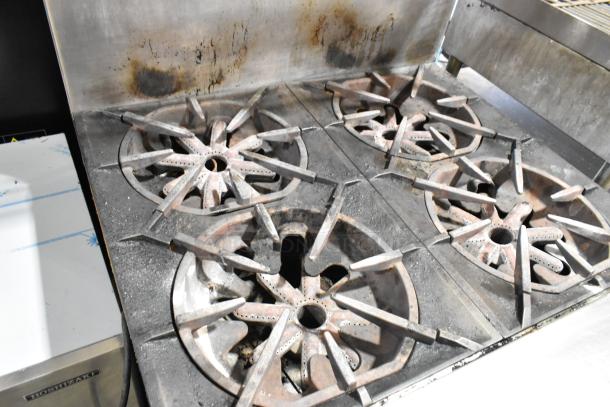 Garland M44R stainless steel gas range with 4 burners, oven, backsplash, and 2-tier overshelf. Shows signs of use.