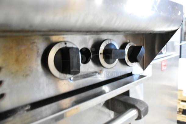 Garland M44R stainless steel commercial gas range with 4 burners, oven, backsplash, and 2-tier shelf. Visible control knobs.