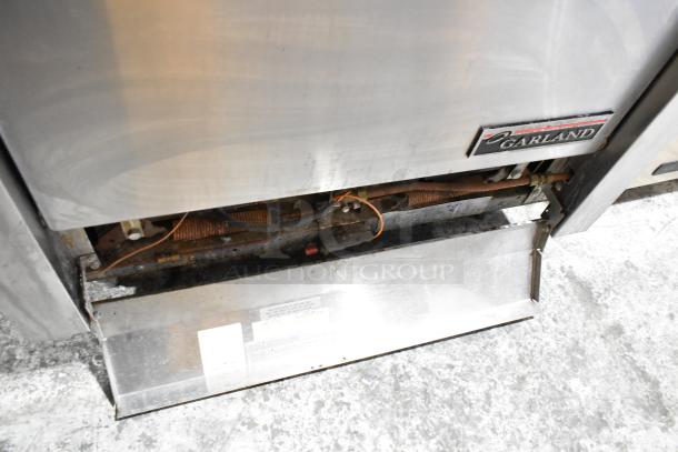 Garland M44R stainless steel commercial 4 burner range with oven, visible brand label, showing lower access and internal components.