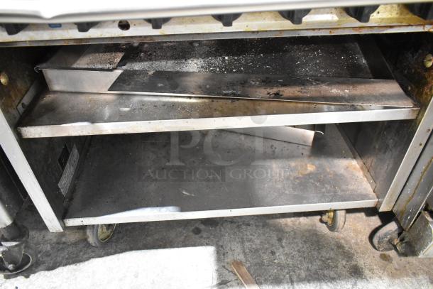 MagiKitch'n 636 stainless steel charbroiler grill with under shelf on commercial casters. Natural gas powered. Visible wear.