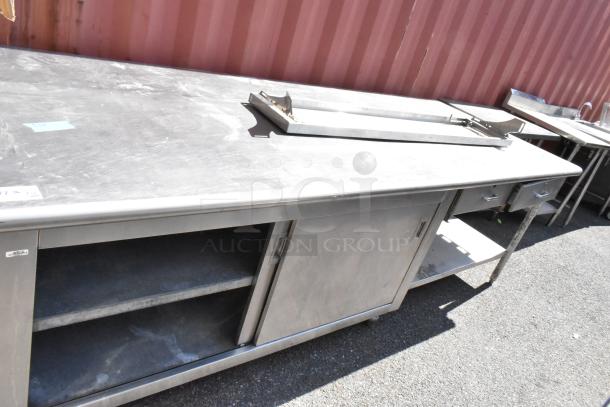 Stainless steel table with under shelves, drawers, and doors. Features include sliding doors and durable surface. Good condition.