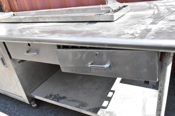 Stainless steel table with under shelves, drawers, and doors. Features durable surface, ample storage, and sturdy legs.