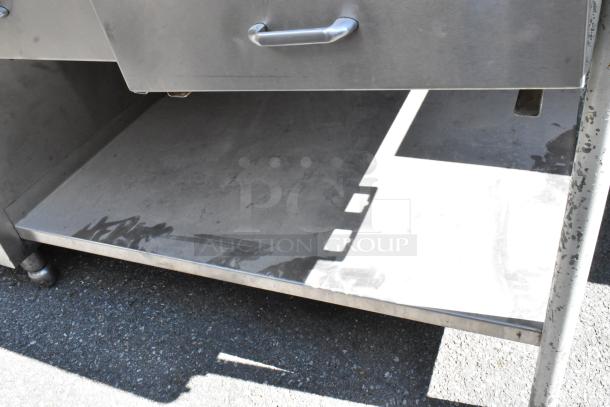 Stainless steel table with under shelves, drawers, and doors; features durable handles; exhibits minor surface wear.