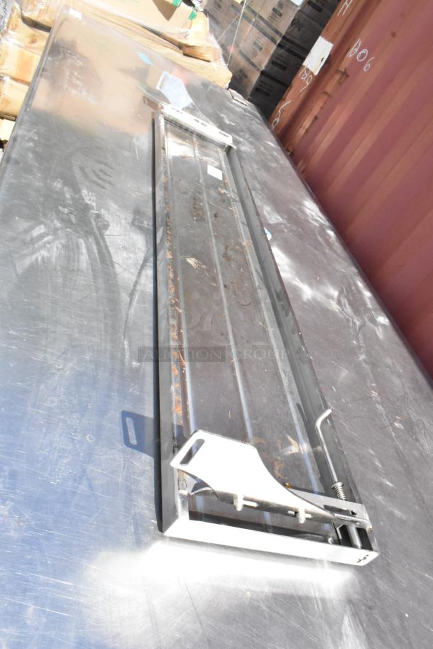 Stainless steel table with visible surface wear, featuring under shelves, drawers, and doors. Lightly scratched top.