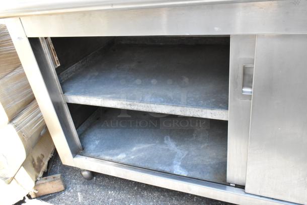 Stainless steel table with under shelves, drawers, and sliding doors. Features sturdy construction, visible wear, ideal for storage.