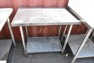 Stainless steel table with metal under shelf, moderate wear, suitable for industrial or kitchen use, sturdy construction.