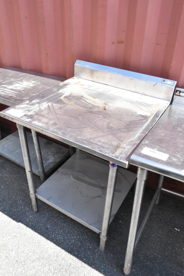 John Boos stainless steel table with metal under shelf, showing surface wear, sturdy legs, and a backsplash attachment.