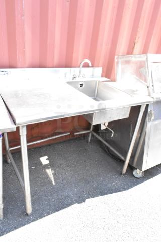 Stainless steel table with integrated sink basin, faucet, and handles. Shows signs of wear, solid construction.