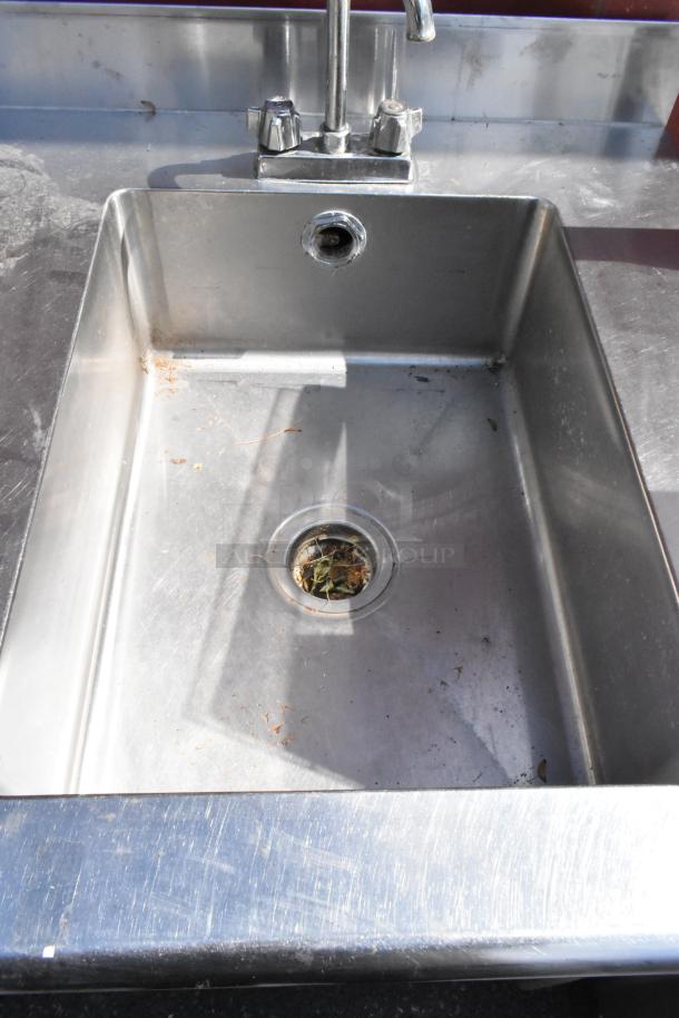 Stainless steel table with integrated sink basin, faucet, and handles. Minor debris visible in sink.