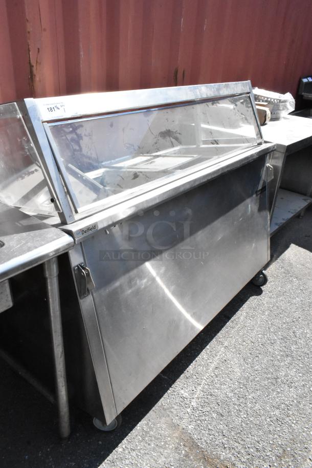 Delfield stainless steel 4 bay steam table with sneeze guard, commercial-grade, on wheels, visible wear, labeled.