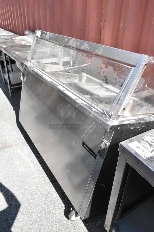 Delfield stainless steel 4 bay steam table with sneeze guard, commercial use, on wheels, slight surface wear visible.