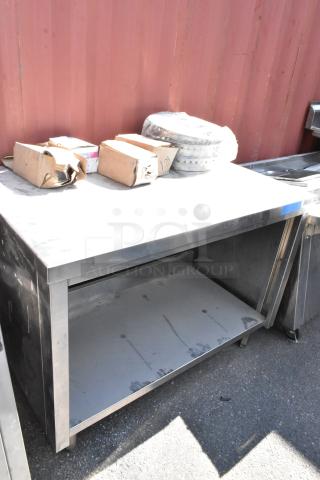 Stainless steel table with metal under shelf, visible wear. Includes cardboard boxes and wrapped contents on top.
