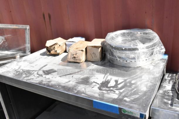 Stainless steel table with metal under shelf, includes boxed contents and wrapped items on top. Brand label: Marlo Mfg. Co.