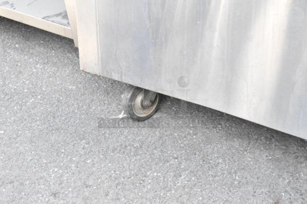 Stainless steel prep table with tray slide, features commercial casters for mobility. Surface shows some wear, ideal for kitchen use.