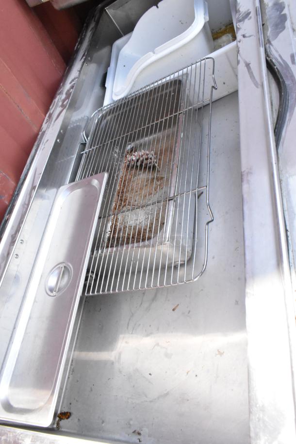 Stainless steel prep table with tray slide, showing commercial casters. Features a metal rack and white trays. Used condition.