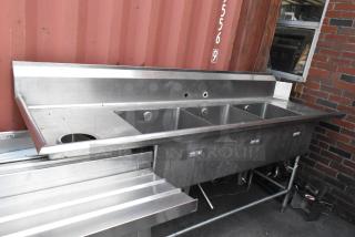 Stainless steel 3 bay sink with left side drain board. Features three compartments, clean surface, ideal for commercial use.