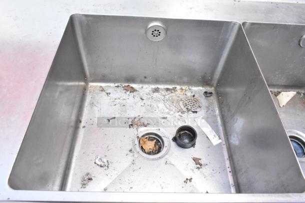 Stainless steel 3 bay sink with left side drain board, showing signs of wear with debris and residue in basin. Ideal for commercial use.