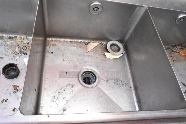 Stainless steel 3 bay sink with left side drain board, showing minor wear and tear, suitable for commercial use.