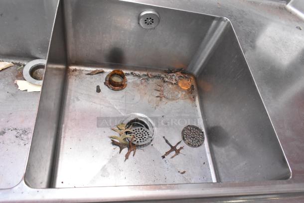 Stainless steel 3-bay sink with left side drainboard, visible wear and debris, suitable for commercial kitchen use.