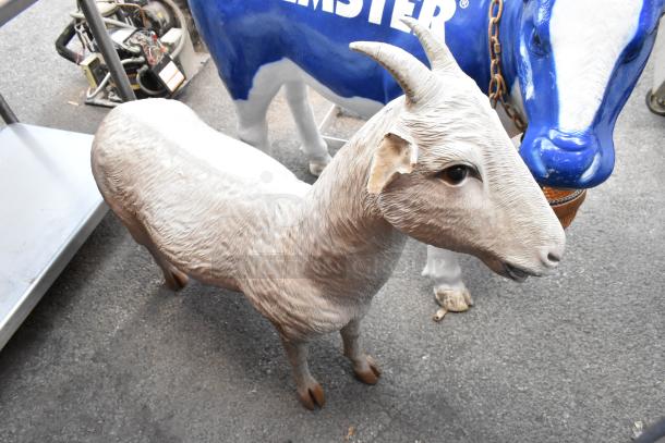 Realistic cow and goat statues on display. Goat features textured fur and curved horns; cow painted blue and white with chain details.