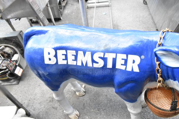 Life-size blue cow statue with "Beemster" logo, white legs, chain necklace, wicker basket, in fair condition.