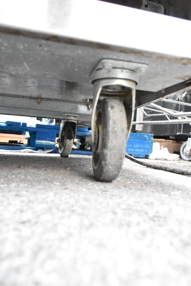 Stainless steel table with two under shelves on sturdy commercial casters, slight wear, suitable for heavy-duty use.