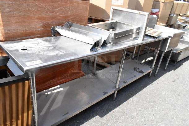 Stainless steel table with under shelf, includes contents, visible wear, hole on top surface, and attached metal components.