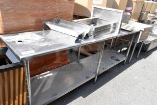 Stainless steel table with under shelf, includes contents, visible wear, hole on top surface, and attached metal components.