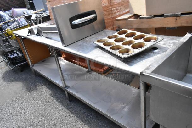 Stainless steel table with under shelf, includes various kitchenware. Appears in used condition, suitable for storage and prep.