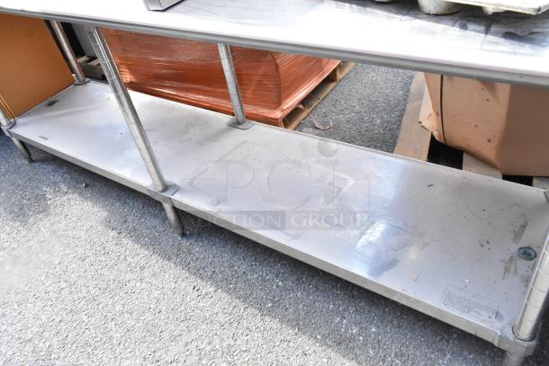 Stainless steel table with under shelf, visible wear. Contains wrapped wood and metal objects. Suitable for storage or workspace.
