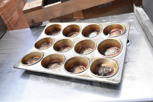 Stainless steel table with under shelf, visible muffin tray with baked goods. Table shows signs of use, ideal for kitchens.