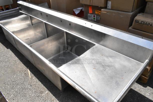 Stainless steel 3 bay sink with dual drain boards, no legs, visible wear. Ideal for commercial use. No visible tags.
