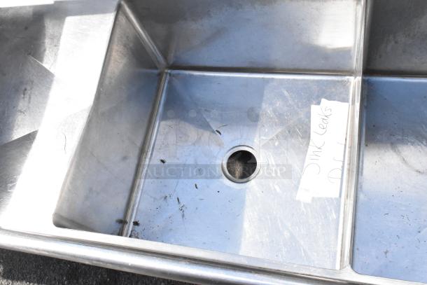 Stainless steel 3 bay sink with dual drain boards, no legs, visible label indicates sink leaks. Used condition.