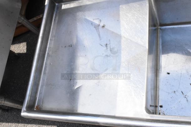 Stainless steel 3-bay sink with dual drain boards, no legs, visible wear, slight scratches, suitable for commercial use.
