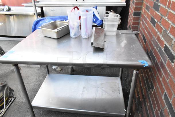 Stainless steel table with under shelf, used condition, includes containers and metal tray. Features durable metal construction.