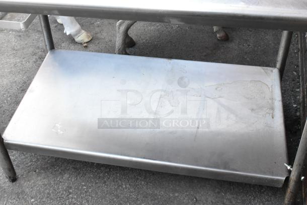 Stainless steel table with under shelf, showing surface wear. Includes various contents. Ideal for industrial use.