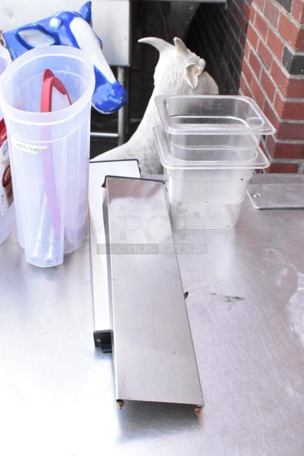 Stainless steel table with under shelf, includes plastic containers and kitchen tools. Clean surface, suitable for commercial use.