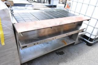 Stainless steel commercial warming table with black tile surface and rust marks, showing signs of use.