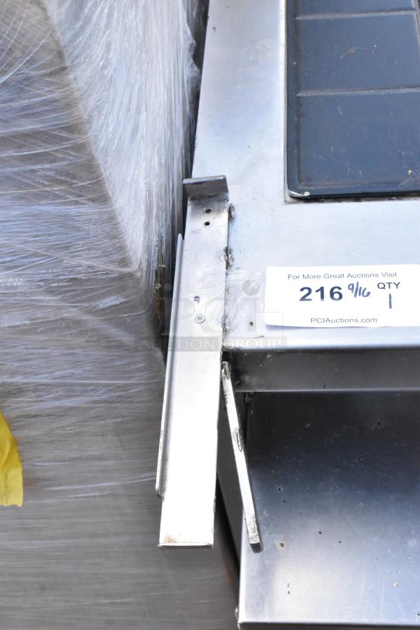 Stainless steel commercial warming table with visible wear, protective wrapping, and label showing auction info and quantity.