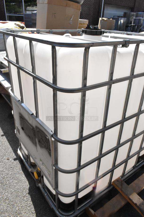 330 GCube Hybrid Pallet, white plastic tank, metal cage frame, large black cap, mounted on a wooden pallet, outdoor setting.