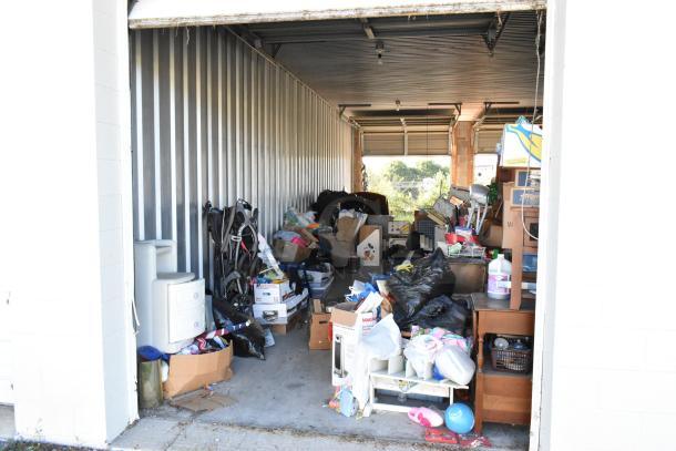 Storage unit #77 packed with a stroller, children's furniture, toys, vintage popcorn cart, Everlast punching bag, tire, rocking chair, and lawnmower.