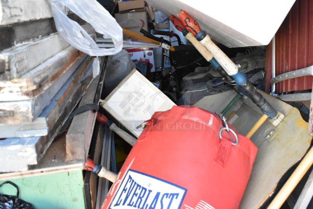 Storage unit contents with Everlast punching bag, stroller, tools, and furniture. Items stacked densely.