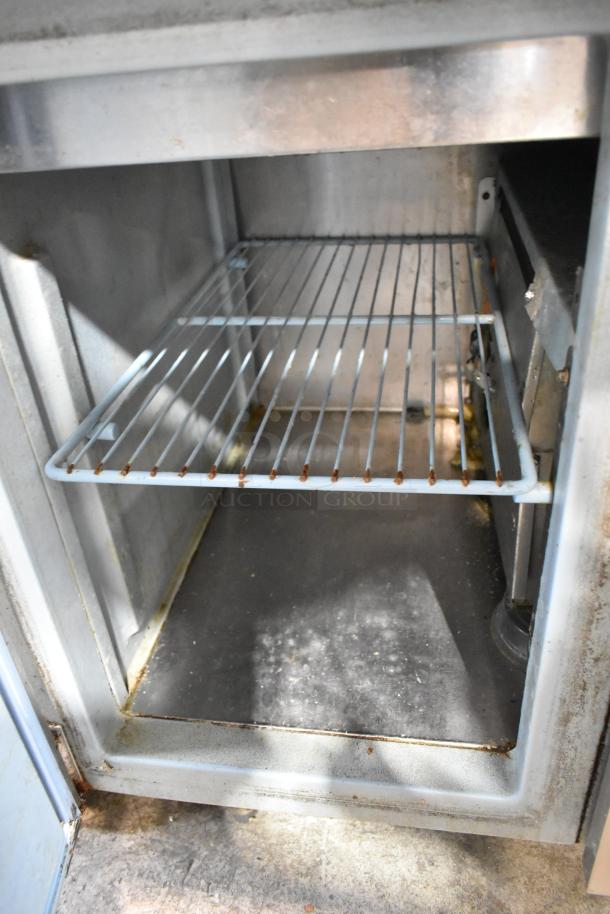 Internal view of Delfield MKV9885751 pizza prep table showing wire shelf and stainless steel lining, moderate wear visible.