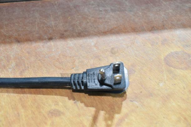 Black power cord plug with visible markings, resting on a wooden surface.