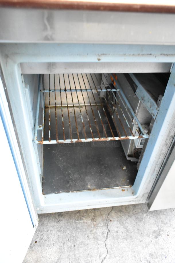 Delfield stainless steel pizza prep table with sink bay, 115V, 1 phase. Interior shows wire shelving. Moderate wear visible.