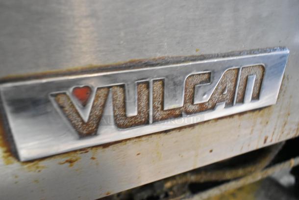 Vulcan logo on a stainless steel commercial gas-powered range with visible wear, featuring six burners and a convection oven.